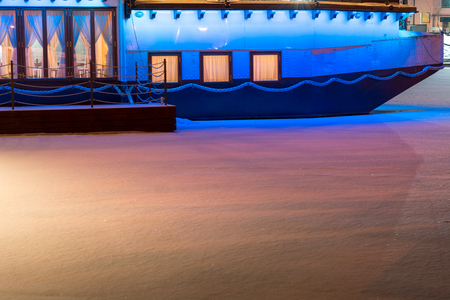 Colorful ship with festive lights frozen in river. Restaurant on water at winter. Atmospheric feeling in city Jelgava at Christmas time.のeditorial素材