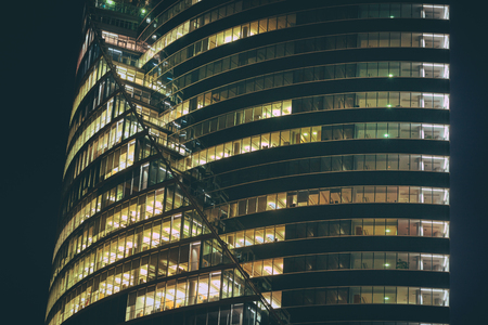 Modern office building made from glass at night time. Lights in the office windows. Modern architecture skyscraper.のeditorial素材
