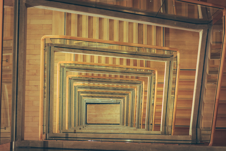 Spiral staircase from above with parquette floor. Square shaped stairs going downwards creating layers from each floor.のeditorial素材