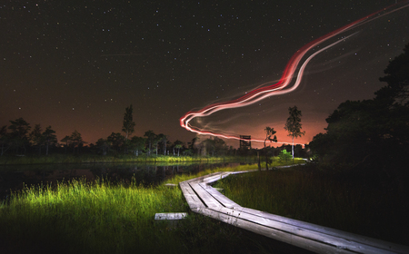 Extraordinary landscape with light painting in night on a wooden trail in swamp. Silhouettes of junipers and reflection in lake. Preserved outdoor territory of Ä¶emeri National park in Latvia.の写真素材