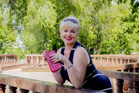 the woman in the park with a red handbag has leaned on a handrailの写真素材