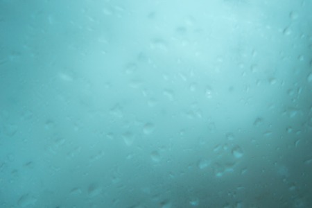 blured water drops on natural misted window glass as abstract background aqua colourの写真素材
