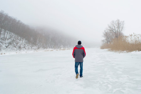 A man walks alone back to camera on a frozen river in winter. Concept of seclusion and retreat.