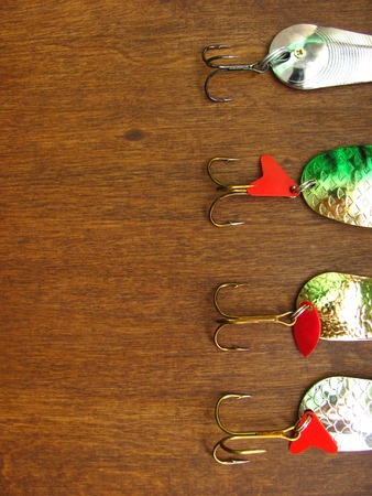 Four shiny artifician baits: details of fishing spinners on a wooden dark background with free space for text. Close up top view. Vertical flat lay.の写真素材