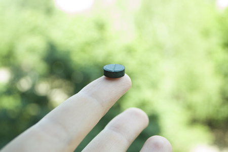 Young woman hand holding a green spirulina tablet against light green nature background.の写真素材