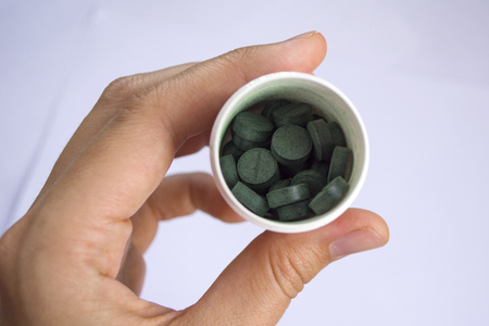 Young woman hand holding a green spirulina tablet in plastic bottle against light background.の写真素材