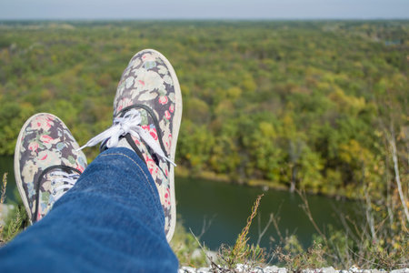 Selfie shooting of female legs. A traveler sits resting on the edge of a canyon above a river...