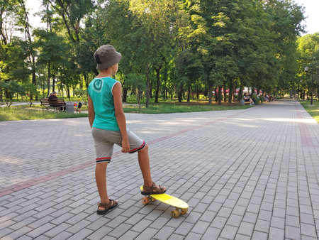 Kramatorsk, Ukraine - 14th July, 2019: Little boy in panama hat and summer clothes on a yellow children's skateboard in the park. Summer activity concept.のeditorial素材