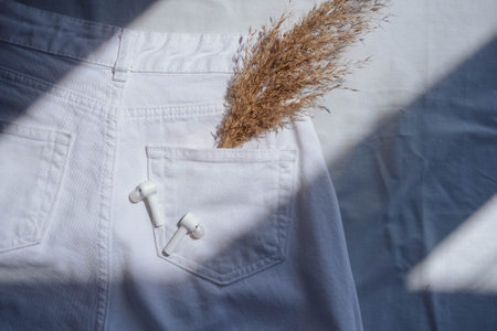 Dry grass in jeans pocket on white background with sun light.White earphones with dried pampas grass in pocket of jeans.pattern,mの写真素材