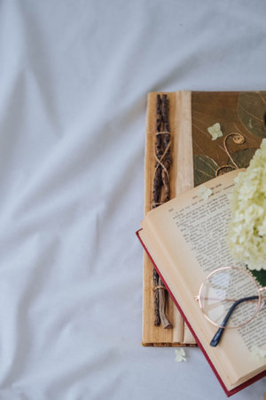 Open book, eyeglasses and hydrangea flowers on white bedの写真素材