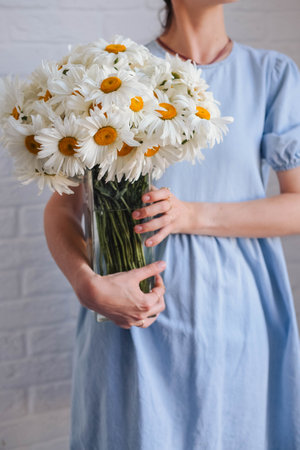 Woman in blue dress holding bouquet of chamomile flowersの写真素材