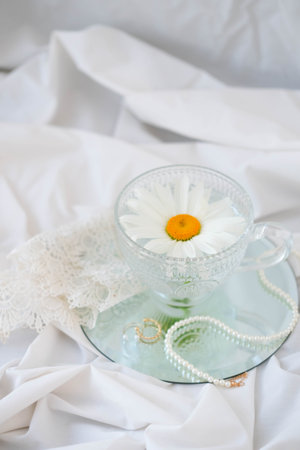 Beautiful chamomile flower in glass cup on white fabric backgroundの写真素材