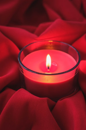Burning candle on a red cloth background. Shallow depth of field.の写真素材
