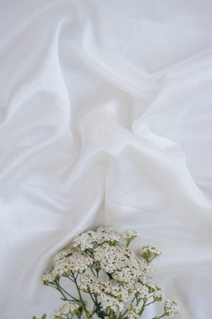 White flowers on a white satin fabric background. wedding concept.の写真素材