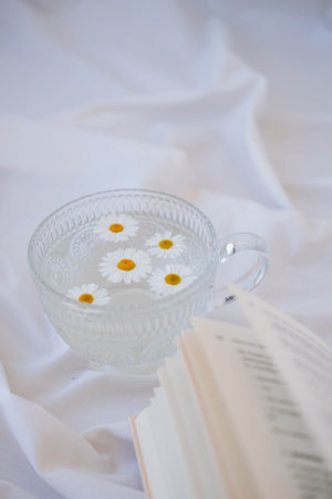 A cup of chamomile tea with book on white fabricの写真素材