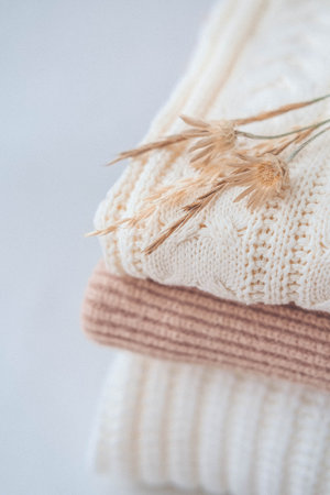 Stack of warm knitted sweaters with dried flowers on white background