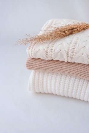 Stack of knitted sweaters with dry grass on white background.