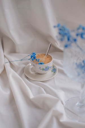 Cup of cappuccino with blue flowers on white fabricの写真素材
