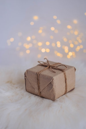 Gift box wrapped in craft paper and tied with twine on white fur background with bokeh.の写真素材