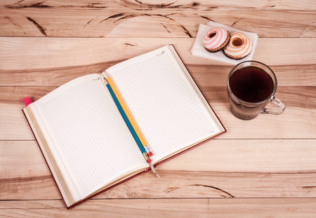 cup of espresso, checkered notebook and bun on wooden background