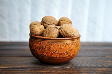 unpeeled walnuts in a pottery on a wooden tableの写真素材