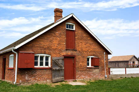 Obsolete brick barn with wooden red doors.  Bluy sky and green grass.の写真素材