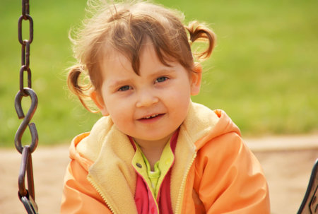Little girl at park playground. Green grass  background. Spring time.