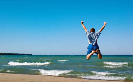Happy man jumping over sea. Sand beach and blue water. Summer, vacation.の写真素材