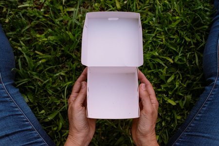 empty white box in the hands of woman sitting on the grass