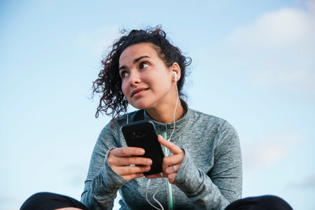 athletic and happy young latin girl with her cellphone with headphones, resting after exercise