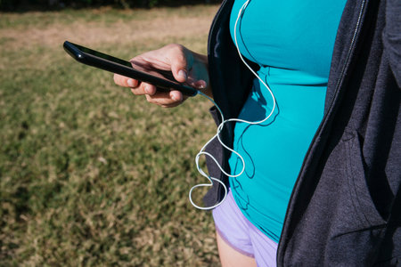 white, caucasian, latin woman, with shorts and sportswear, grabbing a cell phone with headphones,...