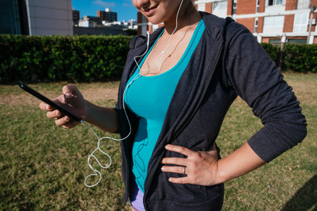 white, caucasian, latin woman using her cellphone with headphones in a park, listening music, with...