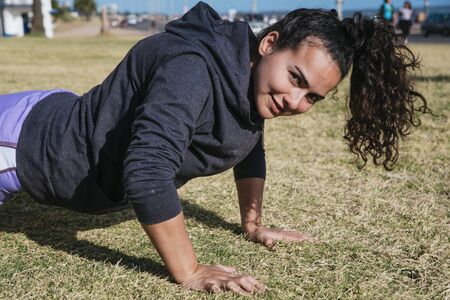 girl working out on the grass doing push ups, with her hair tied and looking at the cameraの写真素材