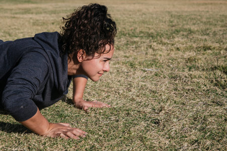 girl working out on the grass doing push ups, with her hair tied and looking forward