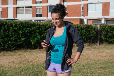white, caucasian, latin woman, with shorts and sportswear, using her cell phone with headphones,...