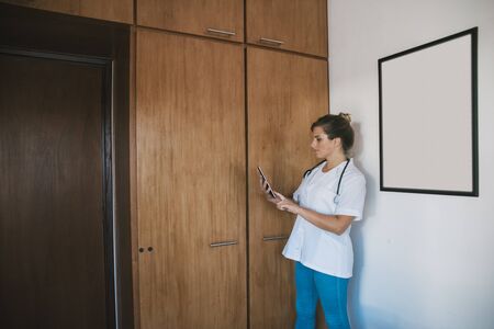 female medical doctor, seriously using a tablet in her office, with stethoscope around her neck and white medical jacketの写真素材