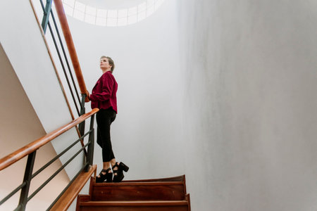 young, white, blond and beautiful businesswoman climbing stairs, with red jacket, black pants and...