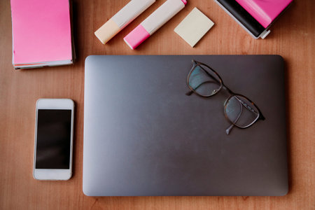 Top view of working space table with laptop, mobile phone, wooden desk, glasses, notebook, sticky...