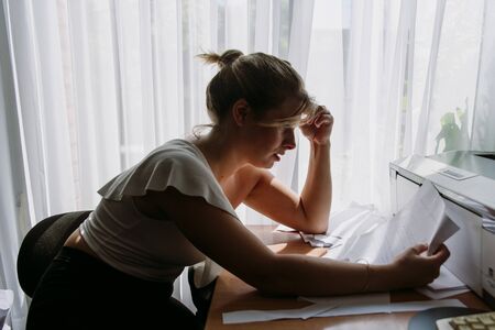 young woman stressed and with headache in the work office space with a lot of papers and things to do, exhausted with the job.の写真素材