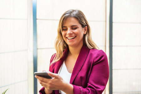 Happy young woman doing a video call with her mobile phone, laughing in the office.