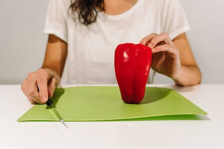 White woman starting to cut a red bell pepper in a green chopping board. Copy spaceの写真素材
