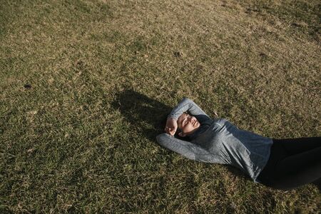 Caucasian girl resting after workout. Athlete lying down on the grass. Healthy lifestyle. Copy space.の写真素材