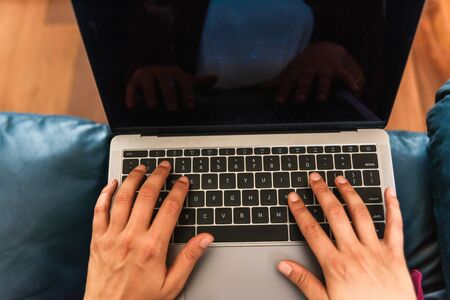 Stock photo of a caucasian woman hands typing on a laptop, on a blue couch.の写真素材