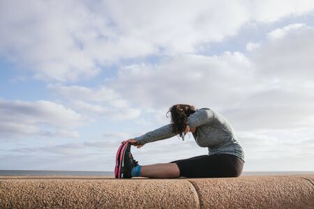 Stock photo of a caucasian woman sitting down stretching her legs. She is wearing sportswear. She is unrecognizable.の写真素材