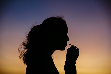 Stock photo of a silhouette of a woman smelling a flower. She is unrecognizable.の写真素材