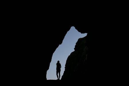 Stock photo of a silhouette of a woman standing in a cave entrance looking up. She is unrecognizable.の写真素材