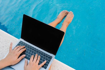 Stock photo from the top of a caucasian woman sitting on the poolside. She is typing on her laptop. She is unrecognizable.の写真素材