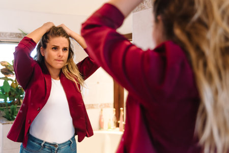 Stock photo of angry caucasian woman looking at herself in the mirror. She is grabbing her hair.