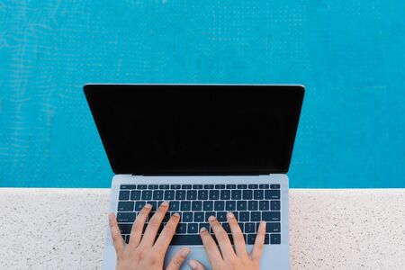 Stock photo from the top of a caucasian woman sitting on the poolside. She is typing on her laptop. She is unrecognizable.の写真素材