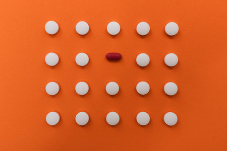 Stock photo of a bunch of pills placed in order on an orange background. There is nobody on the...